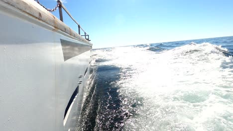 Side-view-of-yacht-sailing-fast-through-ocean-waves-making-foamy-trail