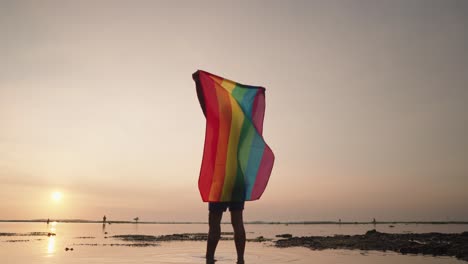 man holding pride flag at sunset beach
