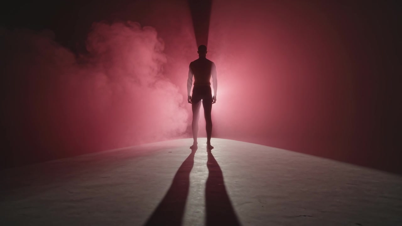 Homem de shorts e regata se movendo, reagindo à luz vermelha que sobe e à névoa que se espalha em um monte elevado.