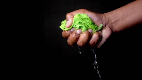 a hand squeezing a wet green cloth over a black background.