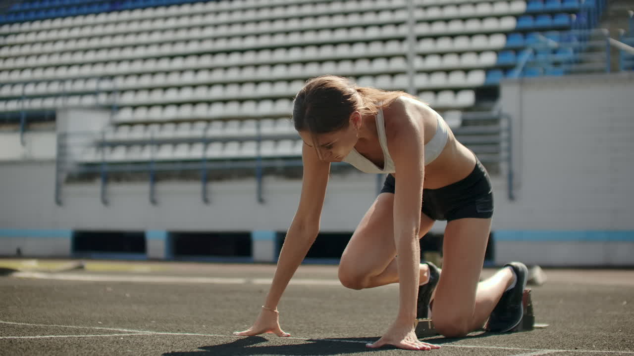 una joven atleta delgada está en posición de comenzar a correr en las almohadillas de la pista en cámara lenta