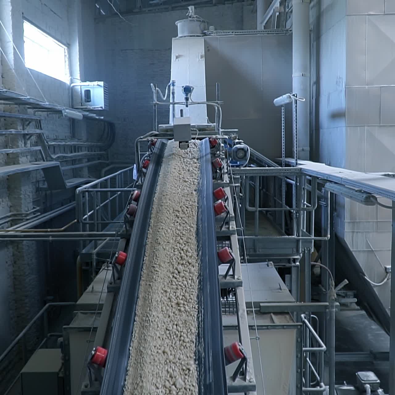 Long sloping conveyor belt moving up to carry the shredded pieces of clay. Industrial plant for kaolin processing