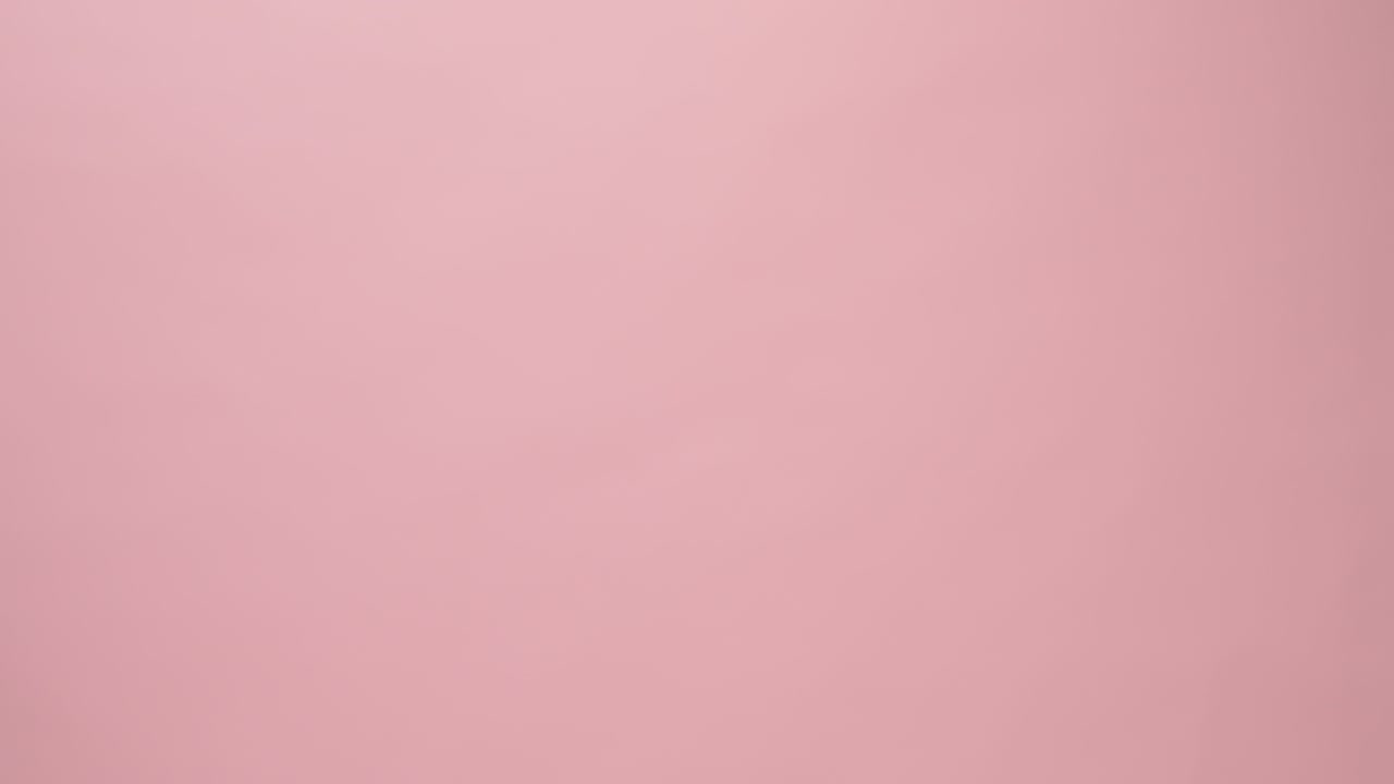 Close Up of hand holding alarm clock on pink background.
