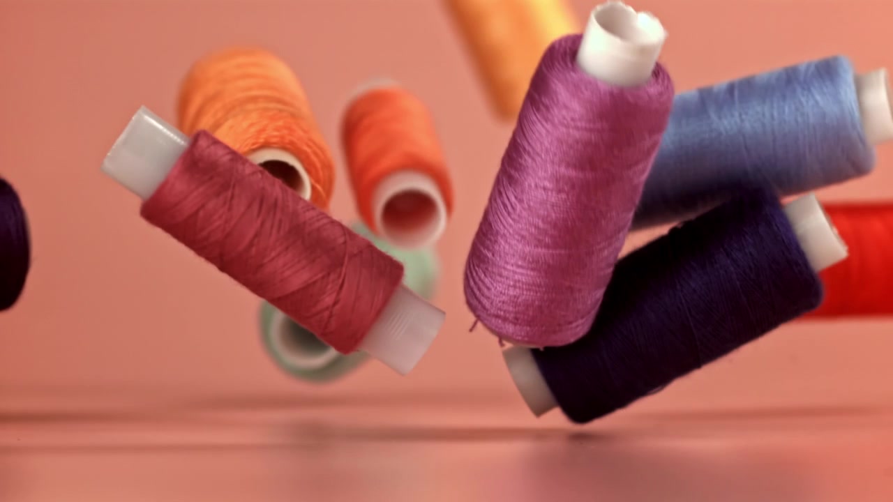 Colorful Sewing Thread Spools Falling in Slow Motion on Pink Background