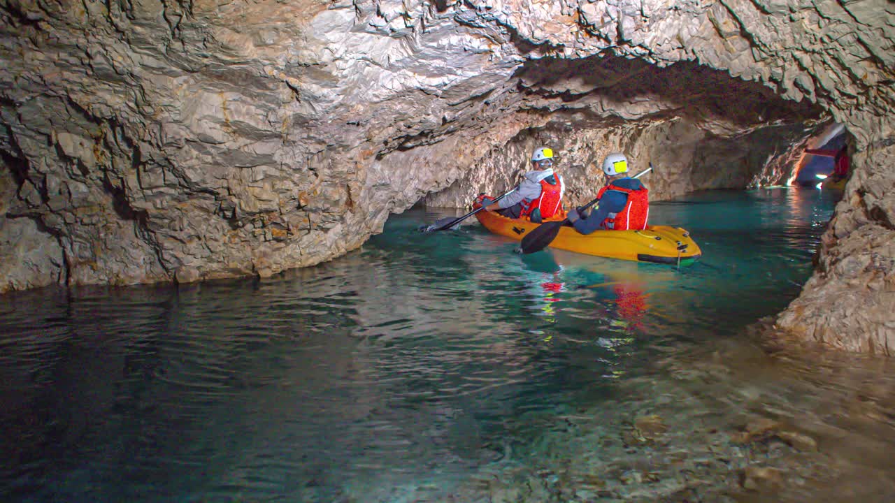 Two young Caucasian boys paddle in underground rocky tunnel on yellow kayak, Podzemlje Pece, Mezica, Slovenia, close up slow motion pan