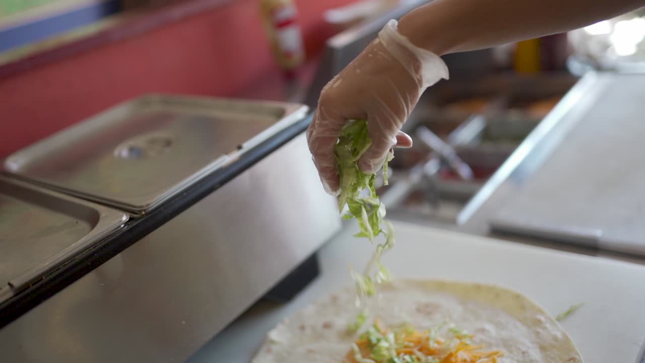 Lettuce being dropped on a soft taco shell in slow motion.