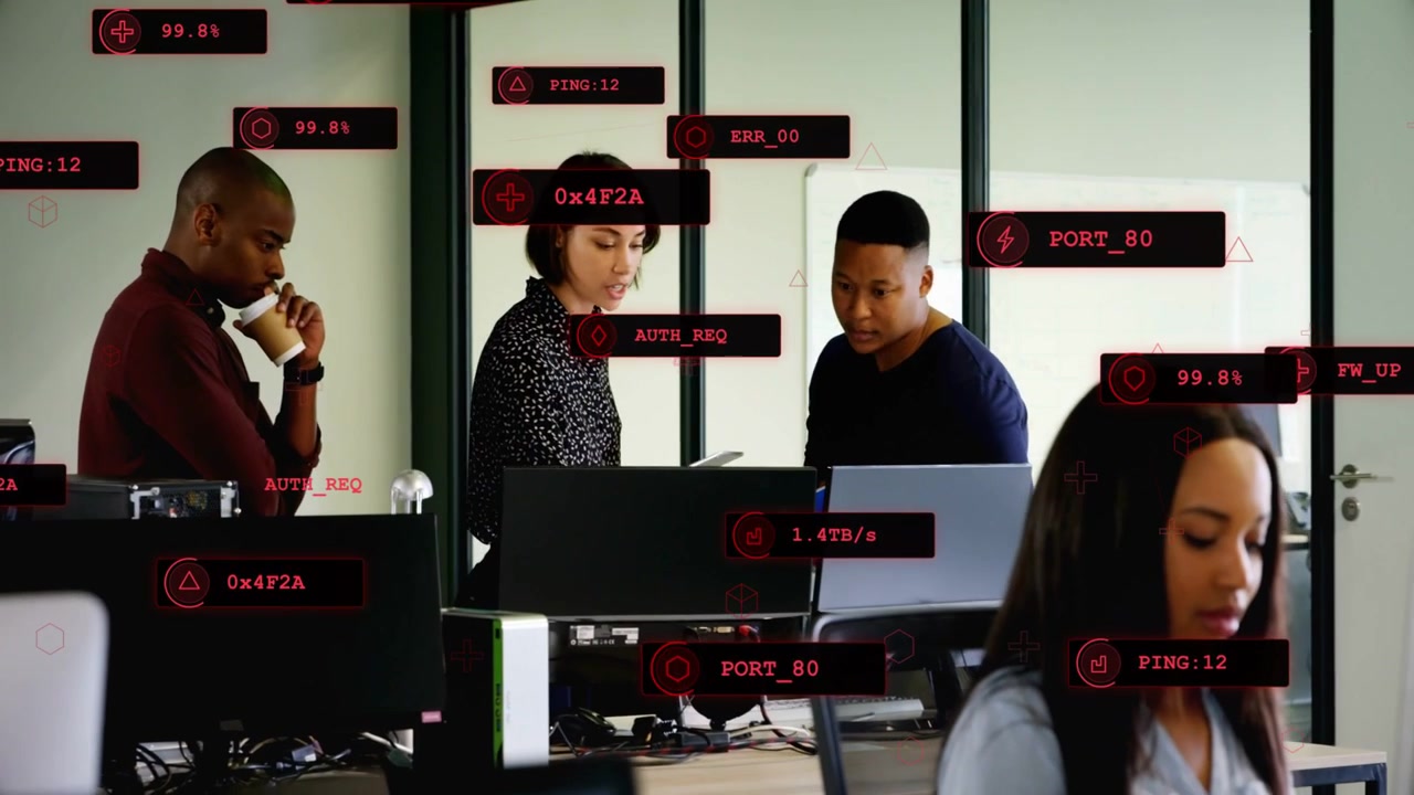 Center woman gesturing to tablet, colleagues leaning in and reading red tags on tech monitors