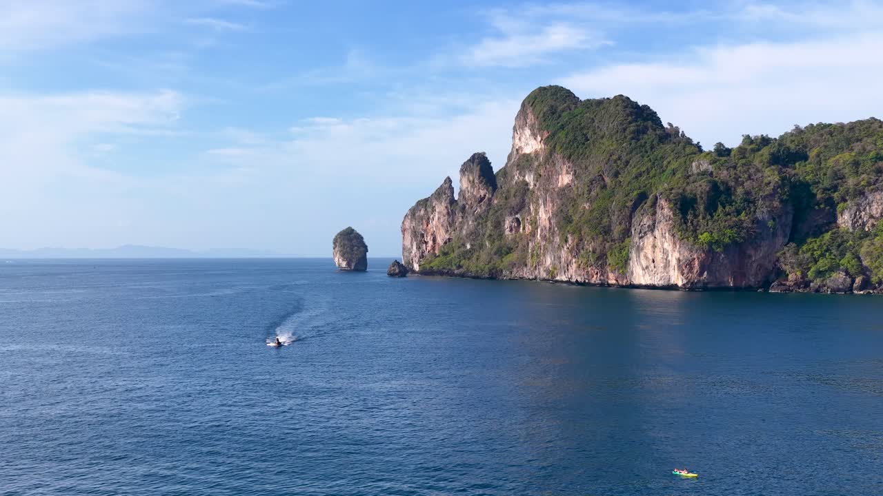 Ampia ripresa aerea di una barca che naviga oltre scogliere calcaree tropicali sotto una luce diurna intensa.