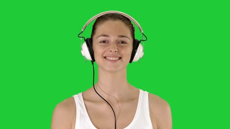 music, people and technology concept - happy smiling woman with headphones walking on a green screen, chroma key