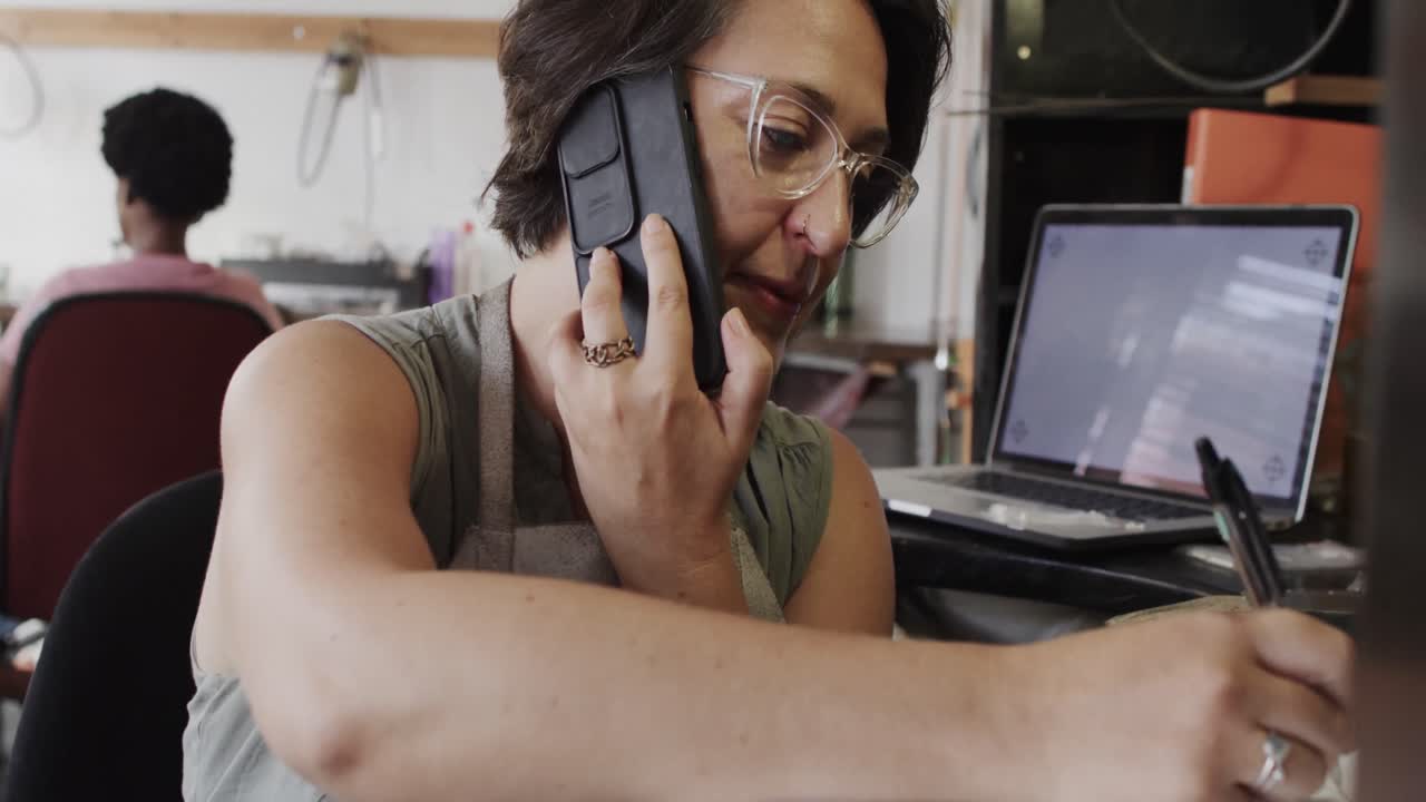 trabajadora caucásica ocupada hablando por teléfono inteligente en un estudio de joyas en cámara lenta