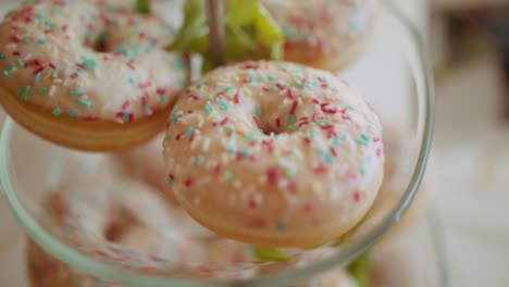 close up on donuts with pink icing and colourful sprinkles on cake stand