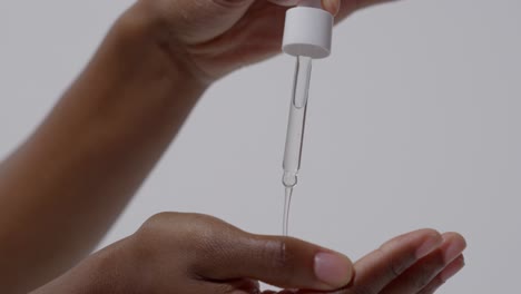 close up of woman squeezing dropper of beauty product onto hand on white background 2