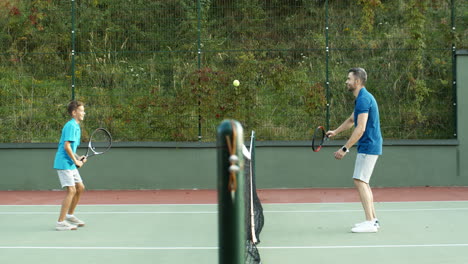 side view of happy father and teen son playing tennis on summer sunny day