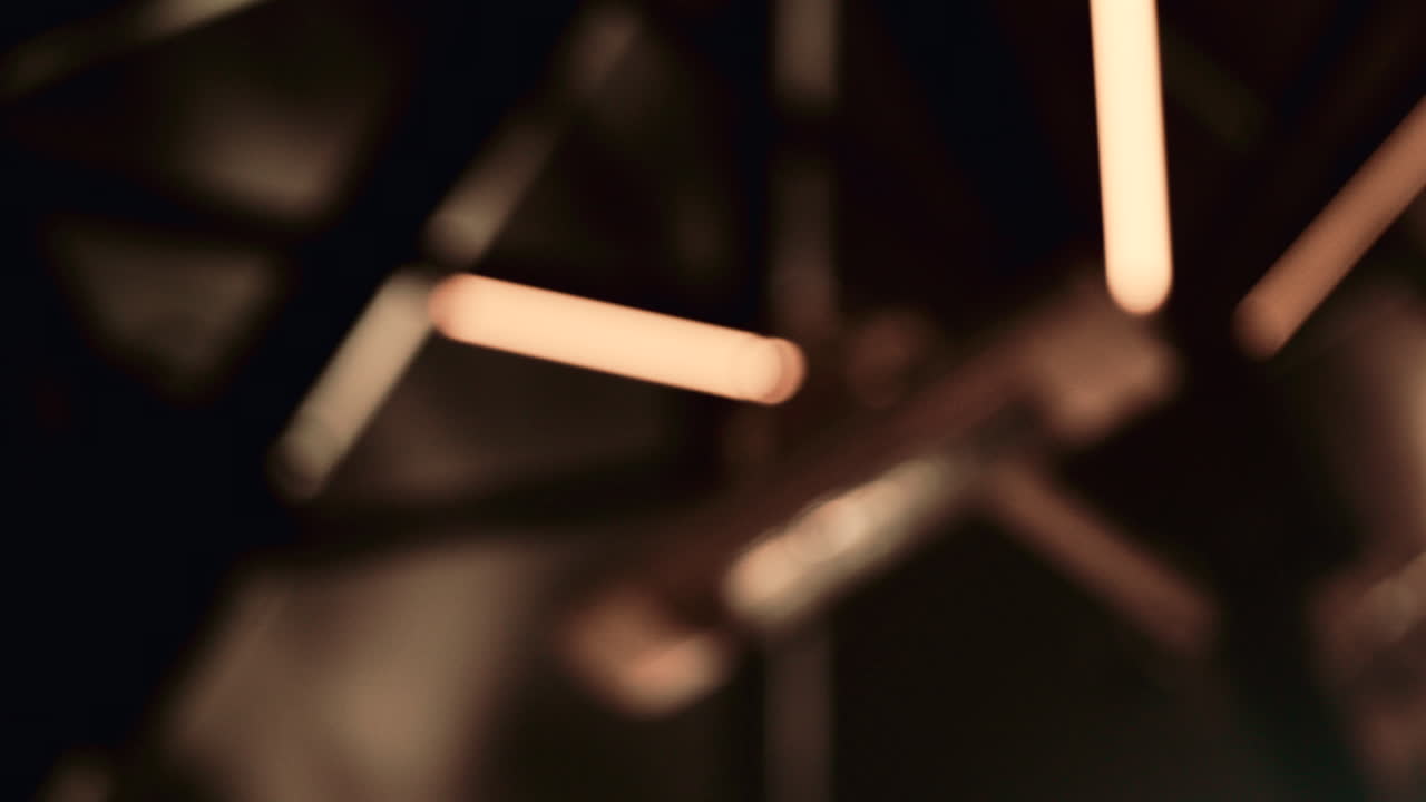 Close up abstract shot of warm linear lights completely out of focus, forming soft glowing shapes on a dark background