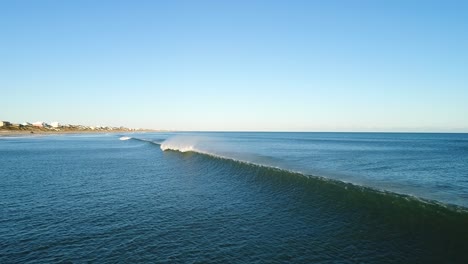 A-stunning-aerial-shot-of-a-massive-wave-chasing-a-drone-to-shore,-following-the-wave-break-to-a-beautiful-rainbow