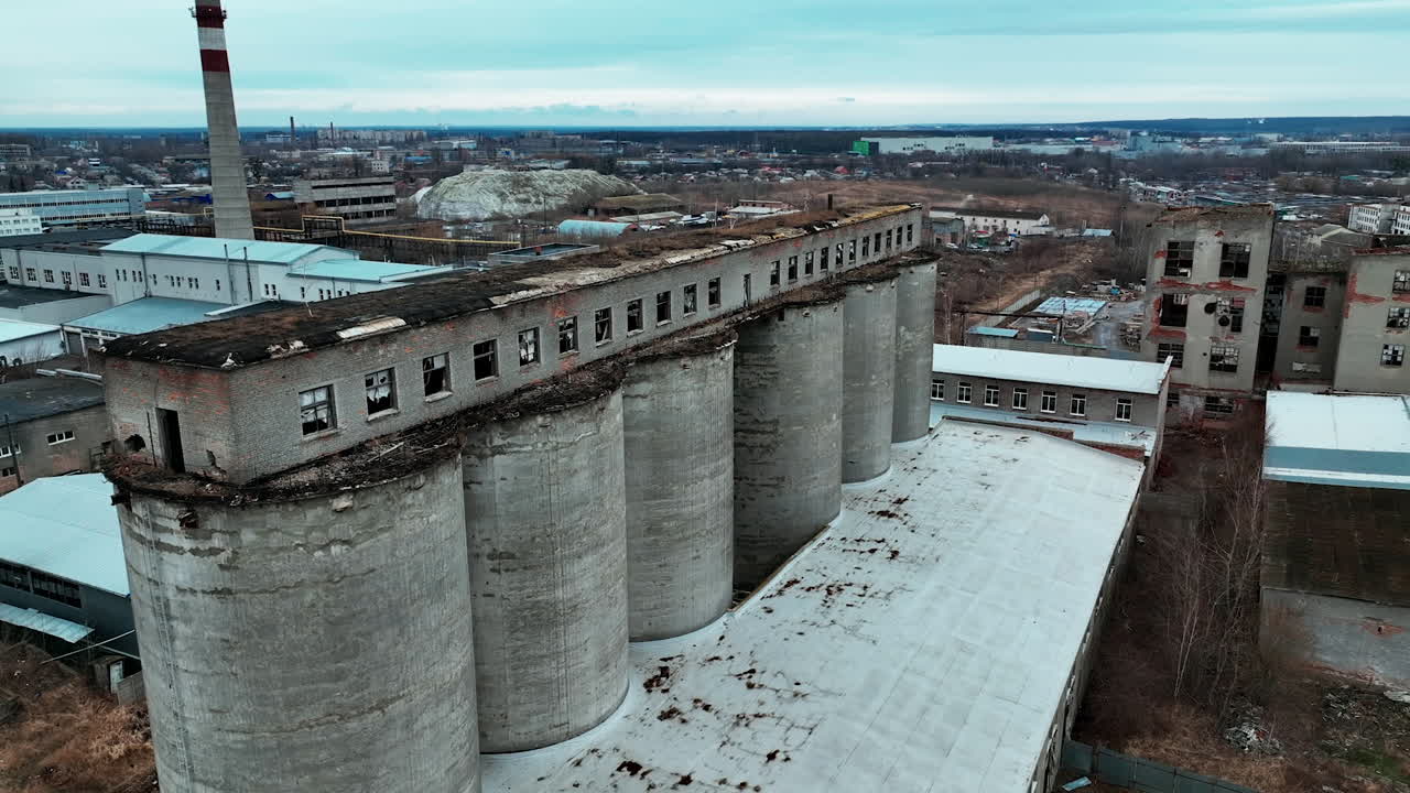 Old chemical plant construction. Ruined long warehouse build on the tops of high concrete reservoirs. Modern industrial plant and city at the backdrop.