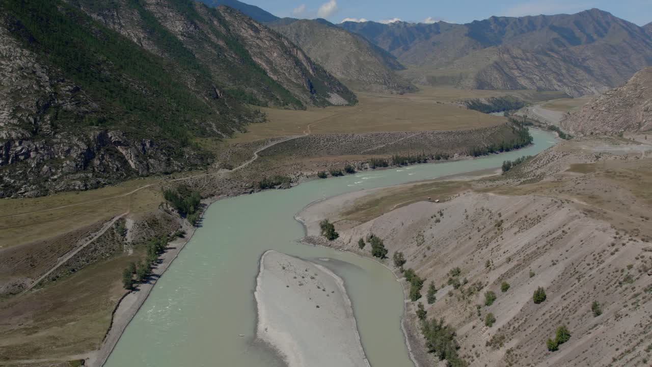 Drone footage of the turquoise Katun River meeting the silty Chuya River in a wide mountain valley near Inya, Altai Republic, Russia, on a sunny day