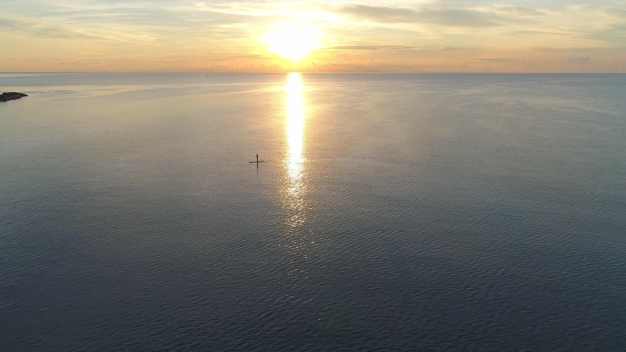 Person paddle boarding in the ocean at sunset