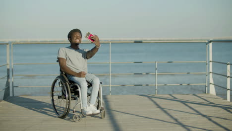 Hombre-Negro-En-Silla-De-Ruedas-Tomando-Selfie-Contra-El-Fondo-Del-Mar