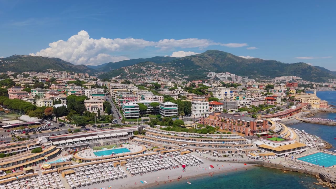 Ripresa aerea della costa di Genova con stabilimenti balneari affollati, piscine ed edifici cittadini