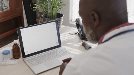 médico afroamericano sentado en un escritorio y usando una computadora portátil con espacio para copiar, cámara lenta