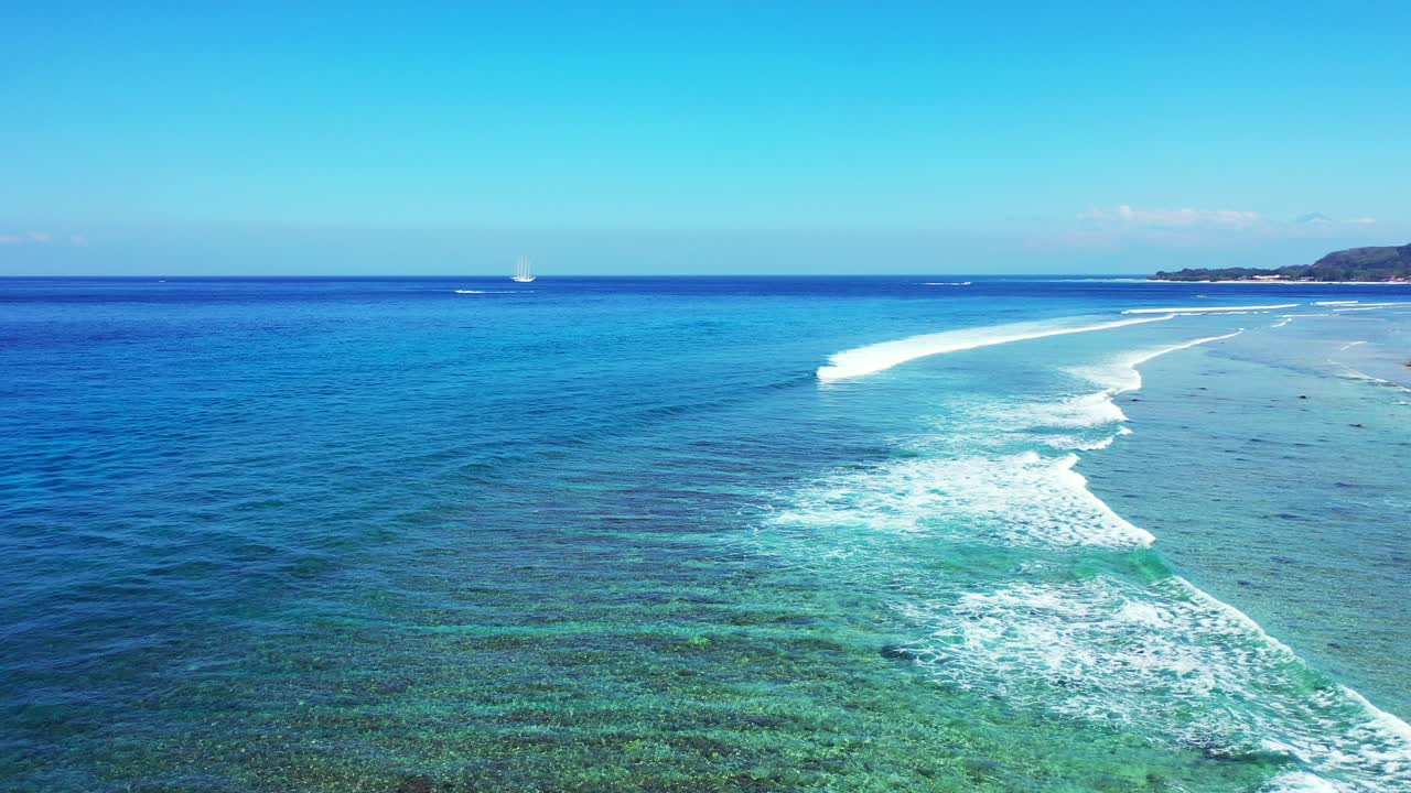 White waves of blue sea splashing over calm turquoise lagoon with coral reefs under clear bright sky, Malaysia