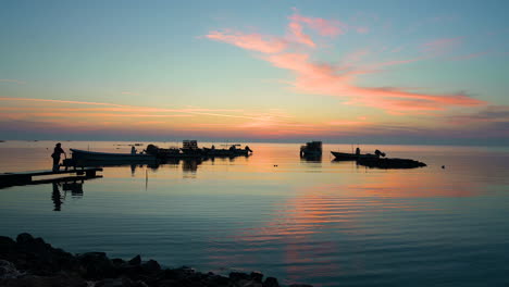 Silhouette-Fischer-Mit-Fischnetzfallen-Auf-Booten,-Die-Auf-Dem-Wasser-Schwimmen,-Mit-Reflexionen,-Die-Zum-Hölzernen-Pier-Kommen,-über-Buntem-Himmelshintergrund-Mit-Sonnenaufgangswolken-In-Der-Dämmerung,-Bahrain