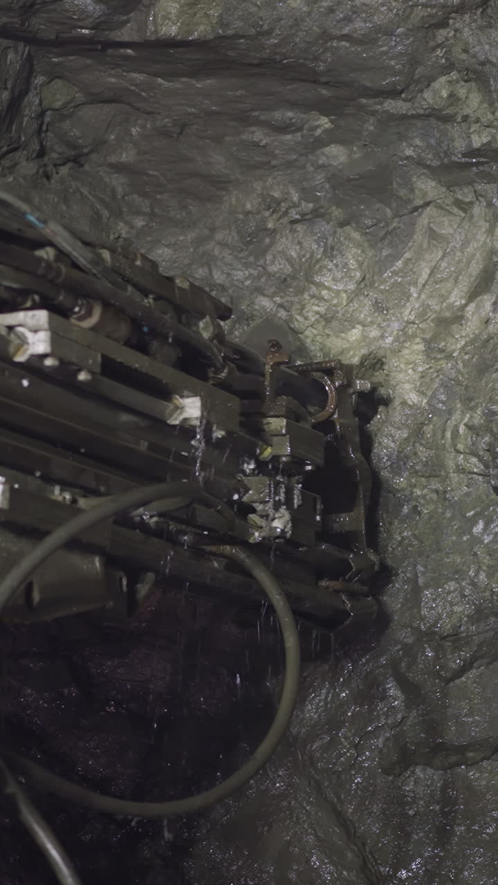 Professional equipment drills holes in rocks of ore mine spraying water. Robot machinery with coolant operates to extract natural resources closeup