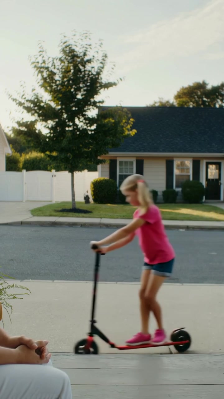 Vertical video: Riding child in pink entering from right, pushing scooter on sidewalk, copy space