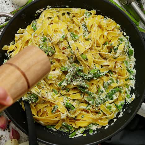 woman adding fresh pepper to homemade tagliatelle pasta with ricotta cheese sauce and asparagus