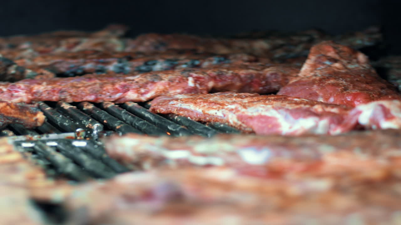 Vista laterale di uno chef che griglia manzo per una festa. Primo piano di un cuoco che fa il barbecue con carne marinata.