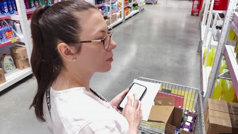 woman with glasses comparing prices and doing calculations on her phone in a supermarket