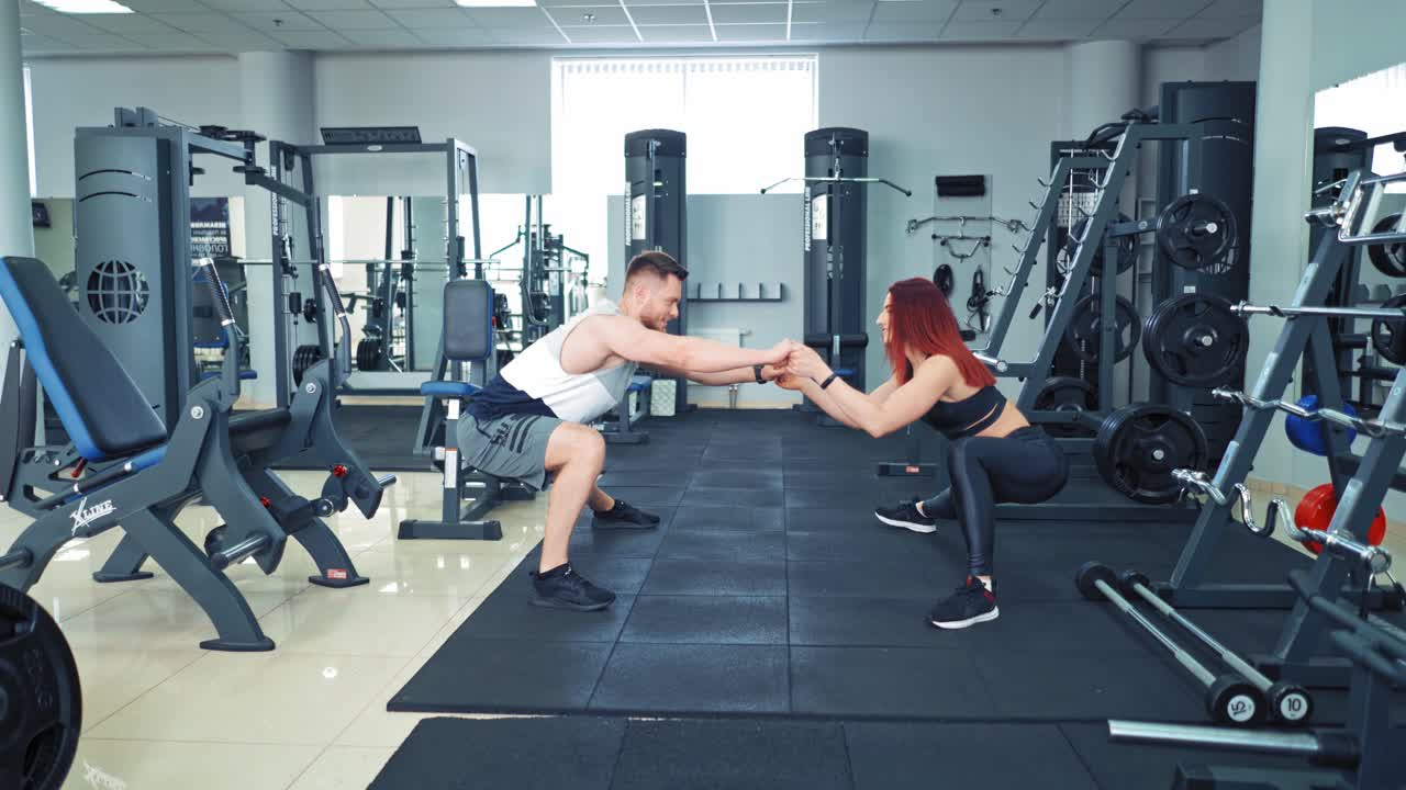 Couple during exercise class at the gym. Close up of focused and motivated strong young fitness couple in sportswear doing squats in the gym