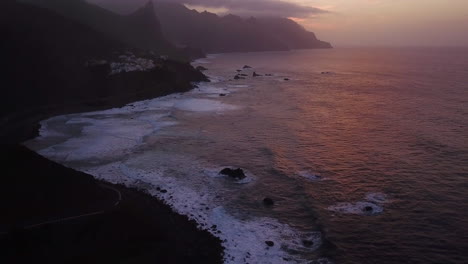 Toma-Aérea-Reveladora-De-Los-Acantilados-Volcánicos-De-Tenerife-Con-Olas-Salpicando-Durante-La-Puesta-De-Sol