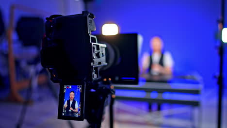 camera display showing the lady talking at the desk at backdrop. blog footage in professional studio. blurred backdrop.