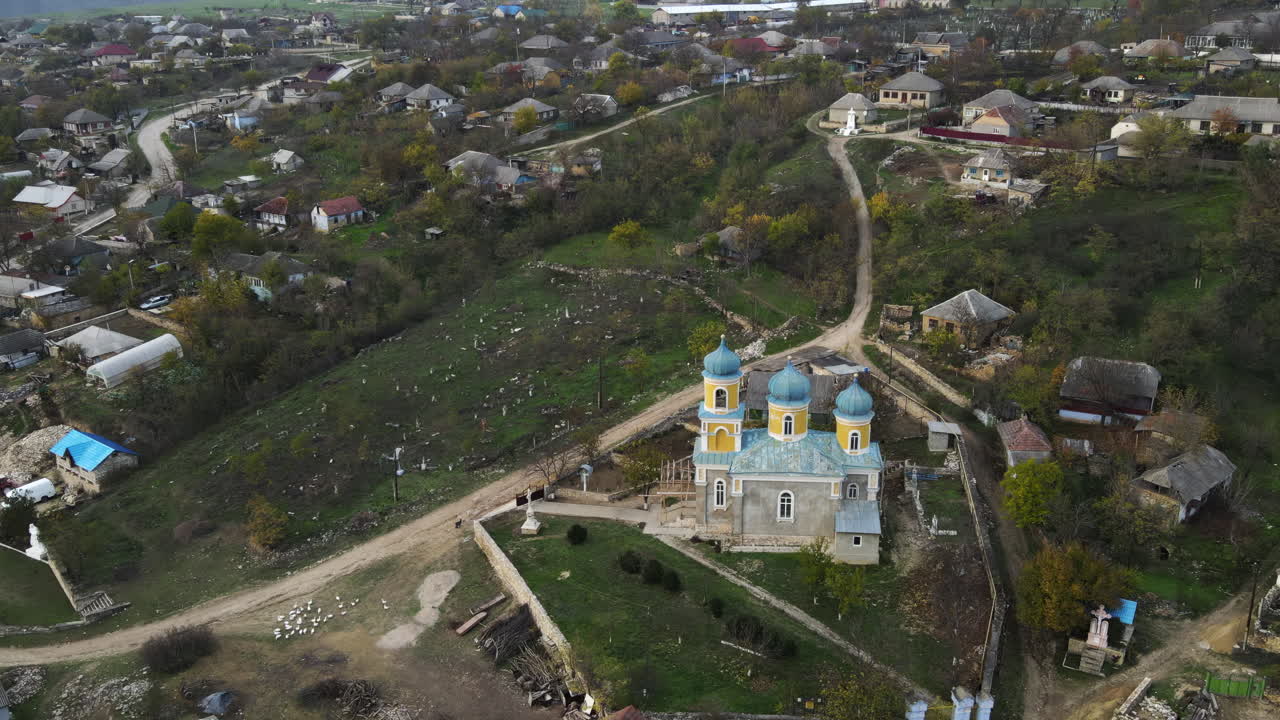 An aerial perspective captures a picturesque village with a vibrant church. Rolling hills and quaint homes create a serene rural atmosphere, showcasing the charm of nature and community