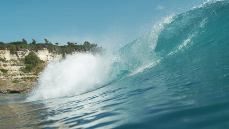 Turquoise wave barrels in toward beach with lush forest background