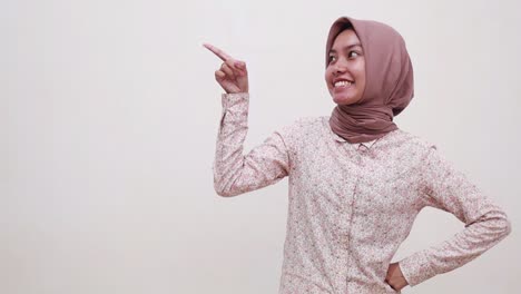 happy wow excited young asian muslim woman standing while pointing and presenting sideways