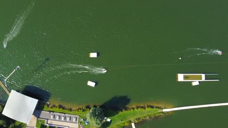 birds eye view drone shot of a waterski system - drone is ascending over the lake with waterskiers and wakeboarders passing by