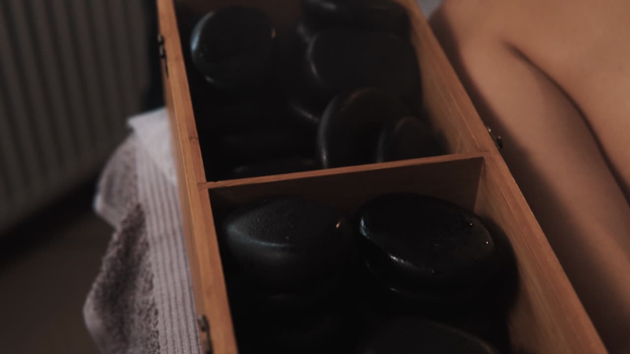 крупный план горячих черных массажных камней, распаренных в деревянном ящике