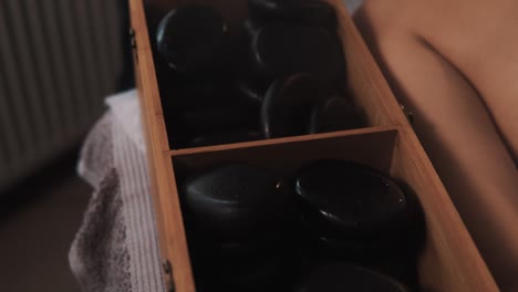 close-up of hot black massage stones steaming in a wooden box