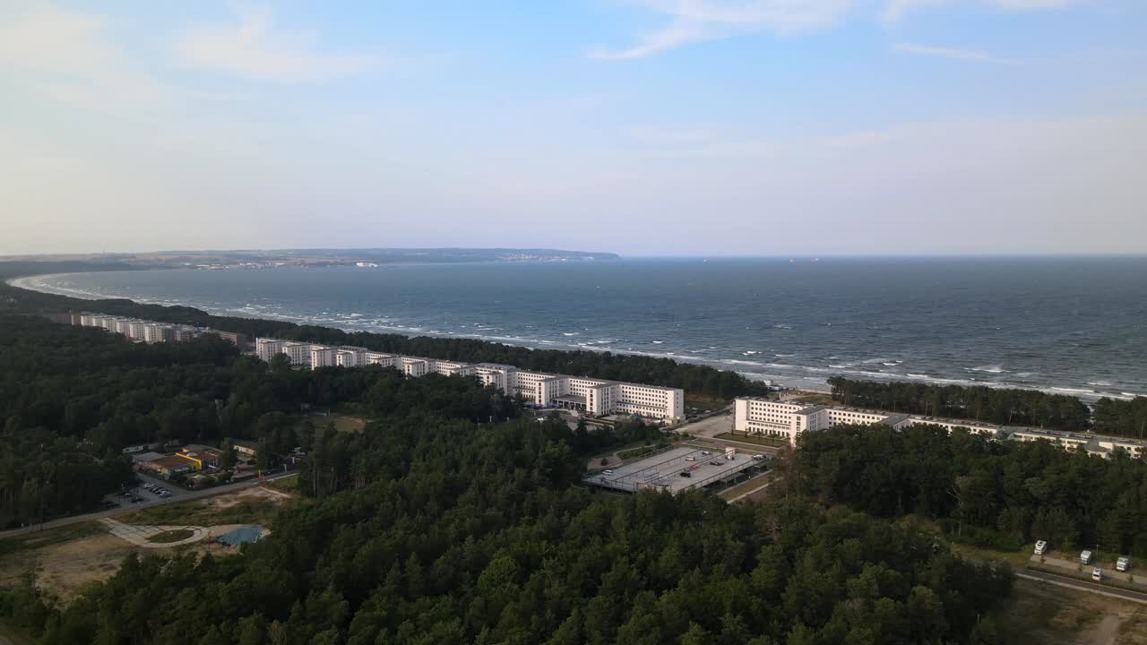 Aerial view of Prora’s historic buildings along Rügen’s coast, facing the vast Baltic Sea with lush forests behind.