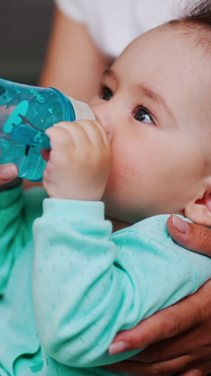 Thirsty little beautiful kid drinking water from a bottle. Caring mom supporting her child and bottle for him. Close up. Vertical video