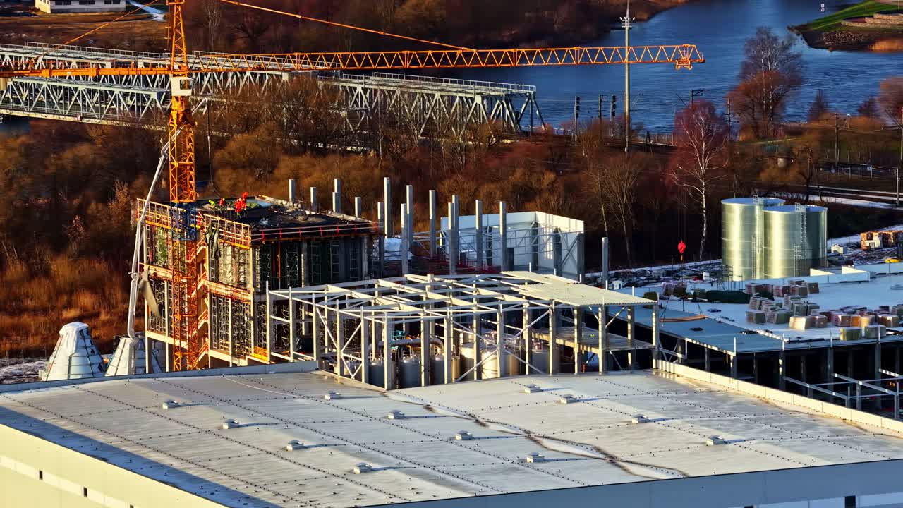 Aerial drone reveals large data center construction site with steel frames, cranes, and active industrial work, early morning sun illumination, establish