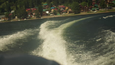 trace track of fast ferry boat on lake water against village on bank closeup. foamy waves behind sailing motorboat on river surface. watercraft riding