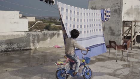 happy youngster playing with the bed sheet that is hanging to dry in the sun while riding his bicycle on the roof