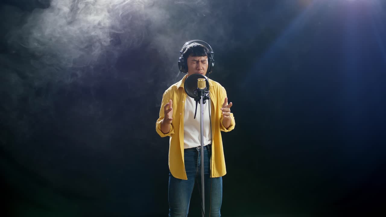 joven asiático con auriculares cantando en un micrófono condensador en el fondo blanco de humo negro