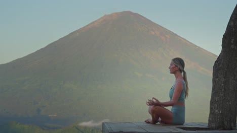mujer meditando en una postura fácil en una plataforma de madera inhalando aire, monte agung