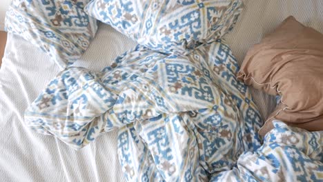 unmade bed with blue and white patterned sheets and pillows