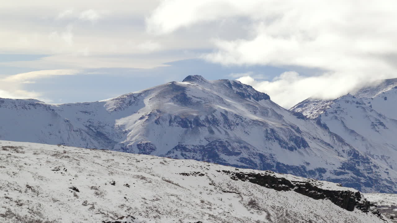 Slow drone pan across the Caviahue–Copahue landscape in Neuquén, Argentina, revealing snow covered ridges and the rounded summit of Copahue Volcano over a windswept valley dotted with Araucaria trees